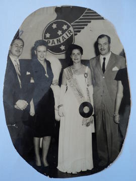 Fotografia de quatro pessoas, dois homens e duas mulheres, sendo que uma delas usa faixa da Rainh...