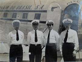 Fotografia de quatro funcionários (tripulantes) da Panair com uma aeronave da Panair ao fundo